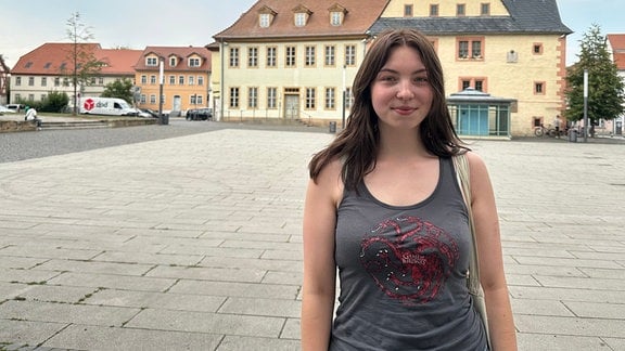 Franziska Kattge steht im Vordergrund des Fotos. Sie hat lange dunkle Haare und mehrere Nasenpiercings. Sie trägt ein dunkles Top mit Game-of-Thrones Aufdruck. Im Hintergrund sieht man den gepflastereten Marktplatz von Sömmerda.