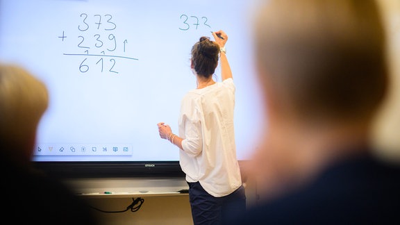 Ein Lehrerin schreibt eine Mathematikaufgabe auf eine digitale Schultafel im Klassenraum