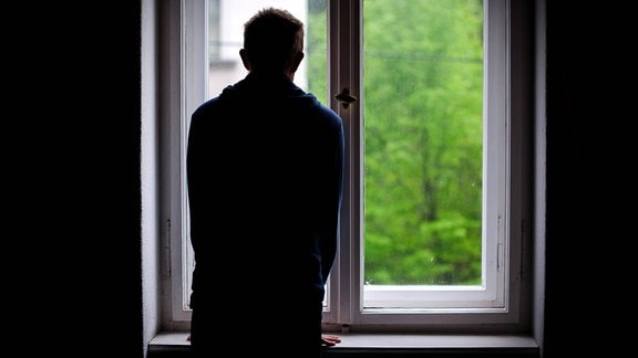 Ein Mann steht allein an einem Fenster und schaut nach draußen.