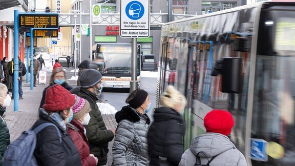 Menschen stehen 2021 mit Mundschutzen an einer Bushaltestelle.
