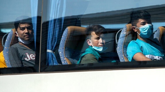 Junge Flüchtlinge, teilweise mit Mundschutz, sitzen 2020 in einem Bus.