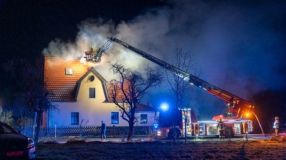 Feuerwehr mit Leiter an einem qualmenden Wohnhaus.