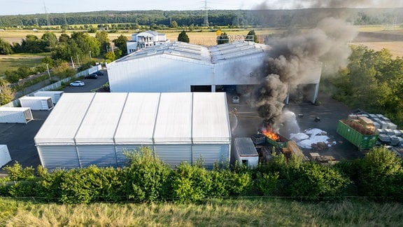 Neben einer Halle steigt Rauch empor.