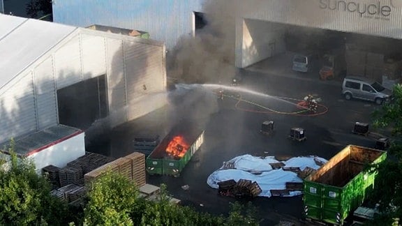 Feuerwehrleute löschen einen brennenden Container auf einem Firmengelände. 