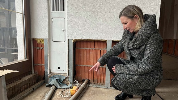 Frau zeigt auf Rohre in Baustelle in Haus