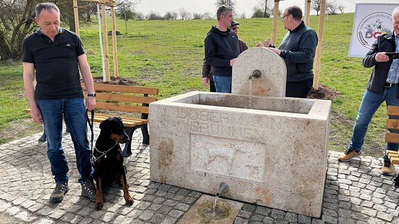 Menschen stehen um einen Brunnen mit Hundemotiv