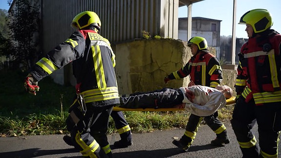 Vier Feuerwehrleute tragen bei einer Übung eine verletzte Person auf einer Trage