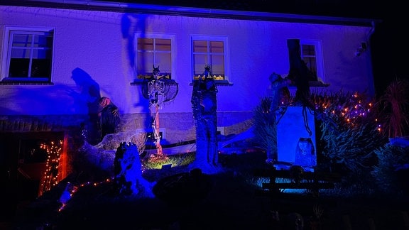 Skelete und ein Grabstein stehen vor einem Haus.