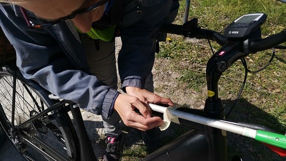 Eine Frau in gelber Weste sammelt am Straßenrand Müll auf.