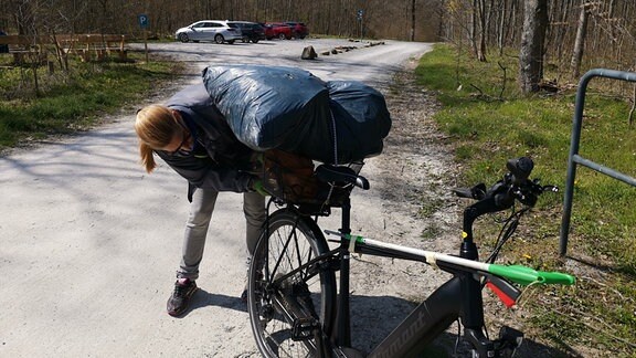 Eine Frau in gelber Weste sammelt am Straßenrand Müll auf.