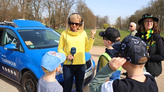 Eine Frau mit einem Mikrofon steht vor Kindern.