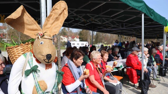 Ein Osterhase steht neben sitzenden Menschen.