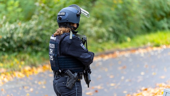 Eine Polizistin mit Helm, schussicherer Weste und einer Maschinenpistole steht auf einer Straße.