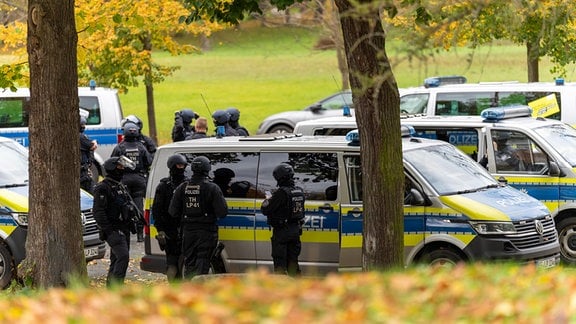 Polzisten mit Helmen und Maschinenpistolen stehen um mehrere Polizeitransproter.