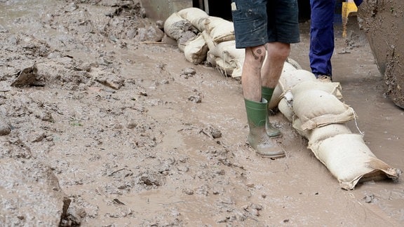 Helfer bauen vor einem Wohnhaus Sandsäcke auf, um Schlamm und Geröll eines Erdrutsches abzuhalten