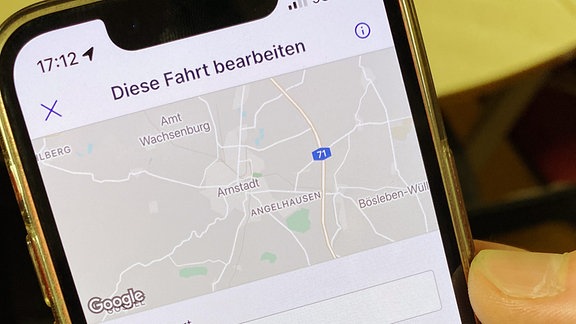  In einer Hand ist ein Handy auf der eine App geöffnet ist. In der App sind Suchfelder.