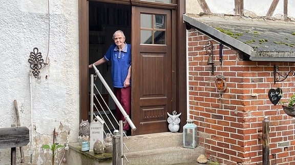 Alte Frau steht an einer Haustür auf einem ländlichen Hof