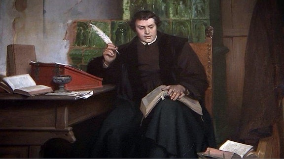 Ein Gemälde zeigt den Reformator Martin Luther an einem Tisch sitzend und ein Buch lesend. 