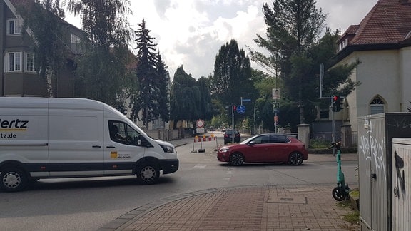 Ein Pkw und ein Transporter fahren über eine Kreuzung. Im Hintergrund ist eine Straßensperrung zu sehen.