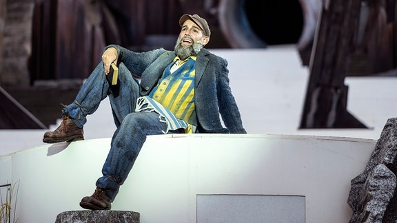 Ein Mann mit Bart sitzt singend auf einer Bühne.