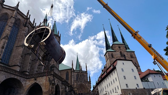 Eine großes Metallrohr hängt an einem Kran der vor dem Erfurter Dom steht.