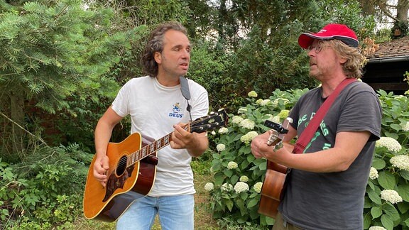 Zwei Männer mit Gitarren in einem Garten.