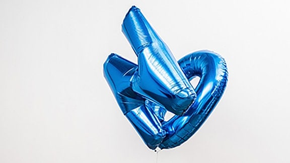 Installation mit zwei schwebenden blauen Luftballons, die an einem Seil an einer im Kreis fahrenden Spielzeuglokomotive hängen.