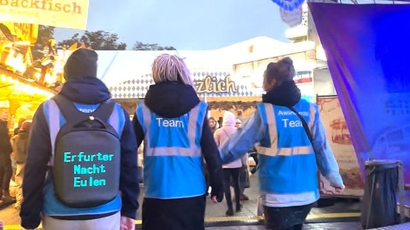 Drei Menschen in bleuen Westen laufen über das Oktoberfest in Erfurt.