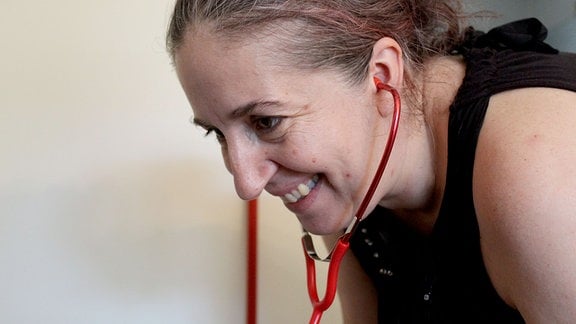 Eine Frau hat ein Stetoskop in den Ohren und lächelt.
