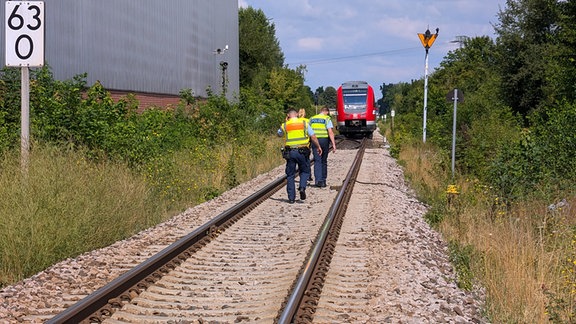 Drei Polizisten auf einem Gleis, dahinter ein Regionalzug.