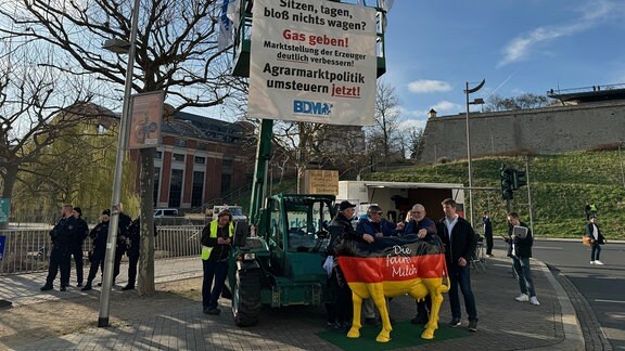 Eine Kuh-Skulptur in Deutschlandfarben, dahinter Bauern die protestieren