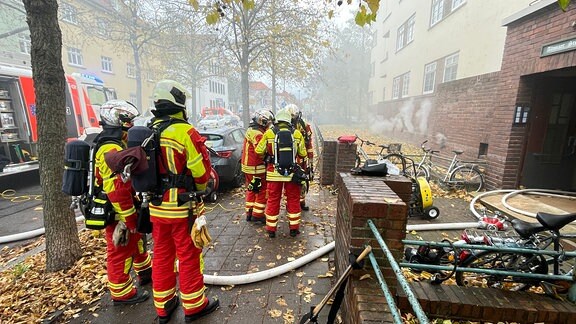 Mehrere Feuerwehrleute stehen vor einem Haus, aus dem Keller dringt Qualm.