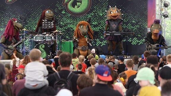 Eine Band in Dinosaurier-Kostümen auf der Bühne.