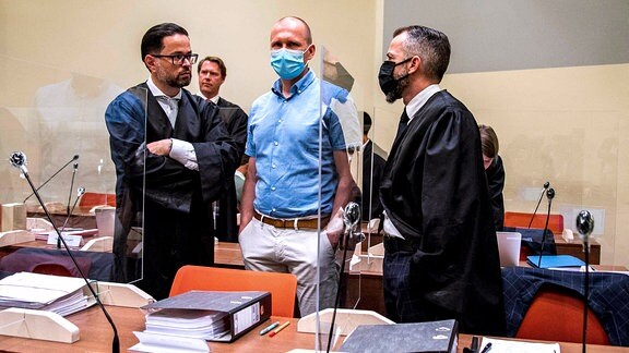 Mark Schmidt (Mitte) steht mit seinen zwei Anwälten hinter Plexiglas im Gericht.