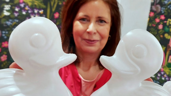 Eine Frau hält zwei weiße Plastikenten hoch.
