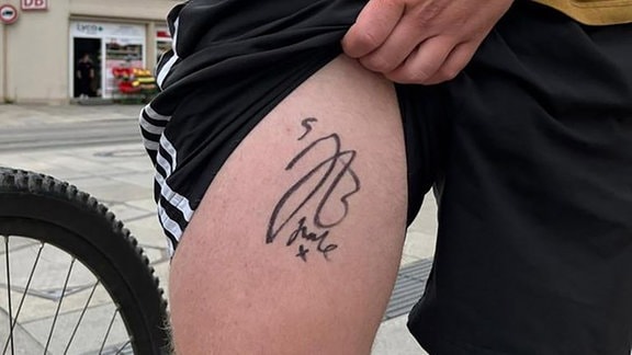Ein Fußballfan zeigt das Autogramm von Fußballstar Jude Bellingham auf seinem Oberschenkel.