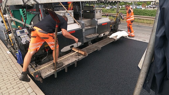 Zwei Bauarbeiter an einer Straßenbaumaschine auf frischem Gummiasphalt