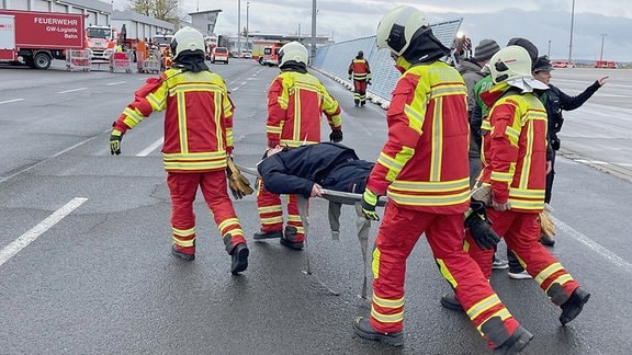 Eine Person auf einer Trage wird von vier Rettungskräften getragen.
