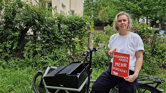 Die Hebamme Susan Küpper mit einem Plakat, auf dem steht "Hebammen haben mehr verdient"