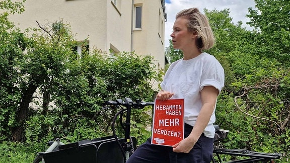 Die Hebamme Susan Küpper mit einem Plakat, auf dem steht "Hebammen haben mehr verdient"