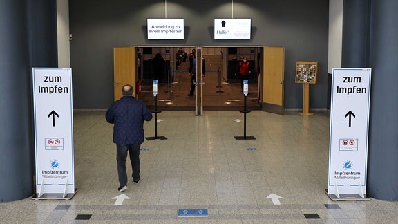 Ein Mann betritt die Messehalle in Erfurt. Hinweisschildern zeigen den Weg