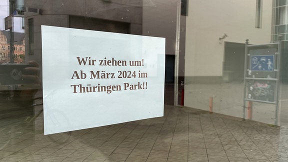 Ein Schild klebt an einem leeren Schaufenster mit der Aufschrift "Wir ziehe um! Ab März 2024 im Thüringen Park!!"