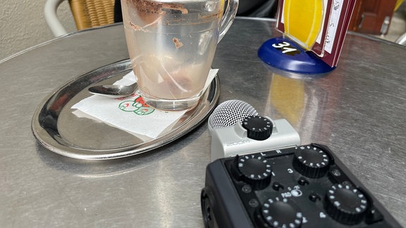 Ein Aufnahmegerät liegt neben einer Kaffetasse.