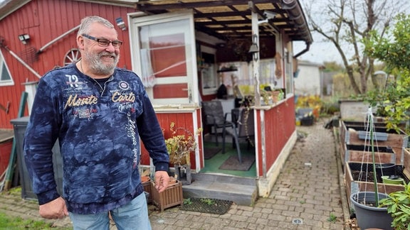 Ein Mann mit Bart und blauem Oberteil in einem herbstlichen Kleingarten. 