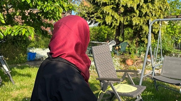 Eine Frau mit rotem Kopftuch sitzt in einem Garten.