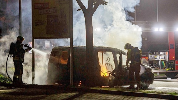Feuerwehrmänner löschen einen brennenden Kleintransporter