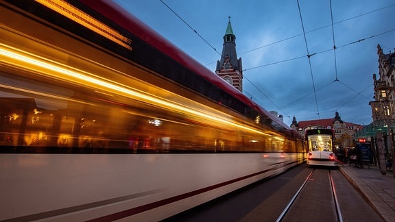 Eine Straßenbahn fährt abends über den Erfurter Anger, die zweite steht an der Haltestelle.