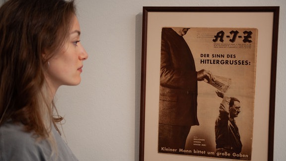 Person sieht sich in einer Ausstellung John Heartfield berühmtes Motiv "Der Sinn des Hitlergrußes" an.
