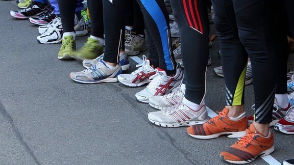 Blick auf das Schuhwerk mehrerer Läufer*innen, die in einer Reihe stehen.