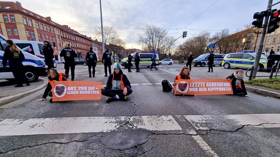 Demonstranten sitzen auf einer Straße, daneben Polizeiautos.